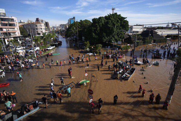 Voluntarios se reúnen para ayudar a los residentes a evacuar un área inundada por fuertes lluvias, en Porto Alegre, Brasil, el martes 7 de mayo de 2024. (Foto AP/Andre Penner)