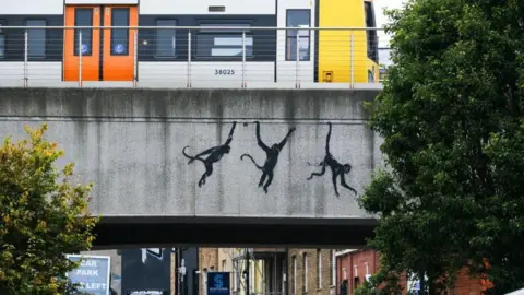 PA Media muestra tres monos negros colgados de un puente ferroviario de hormigón gris en Brick Lane