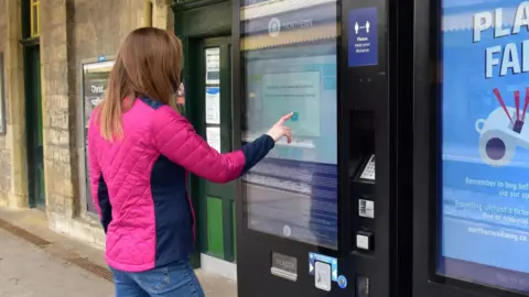 Una mujer del norte con una chaqueta rosa compra un billete en una máquina expendedora del norte